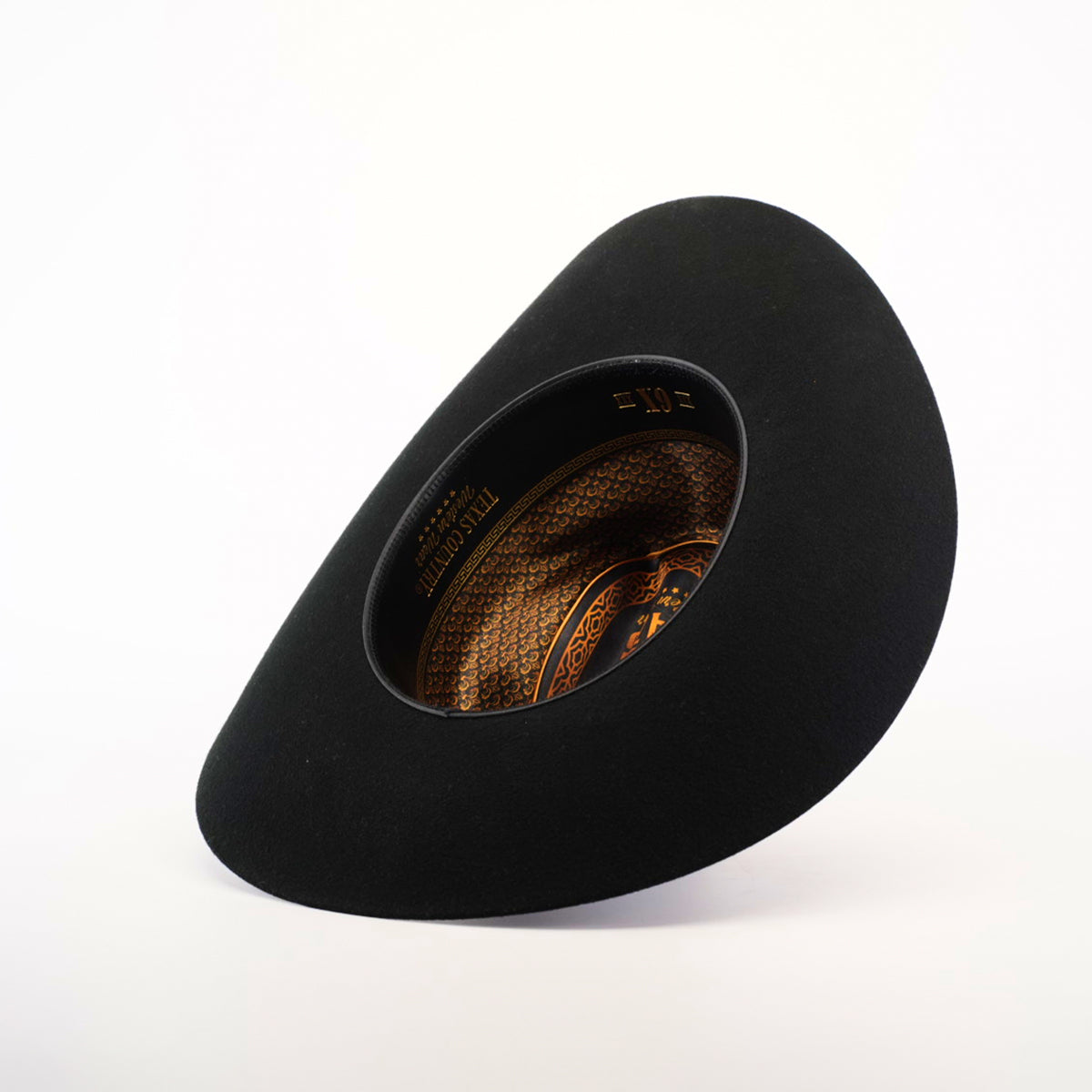 The 6X Sinaloa Black hat, turned on its side against a plain white background, reveals an intricately patterned interior with gold designs and text. Its wide, curved brim embodies Western heritage and contributes to its smooth texture.