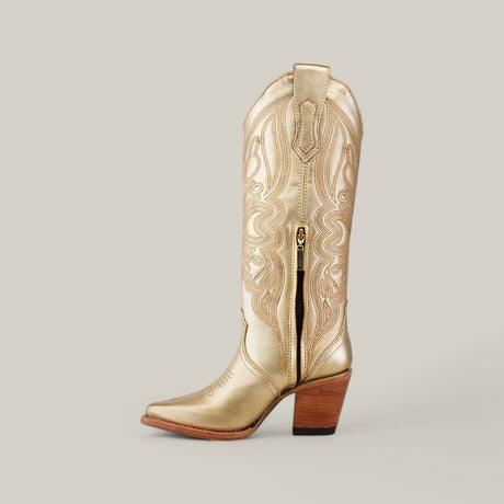 Part of the Platinum Collection, the Linda Tall Shaft Gold - J Toe cowboy boot boasts an intricate embossed pattern and gold finish with a wooden block heel. Set against a light neutral background, its style is elevated by a classic J Toe for a timeless Western appeal.