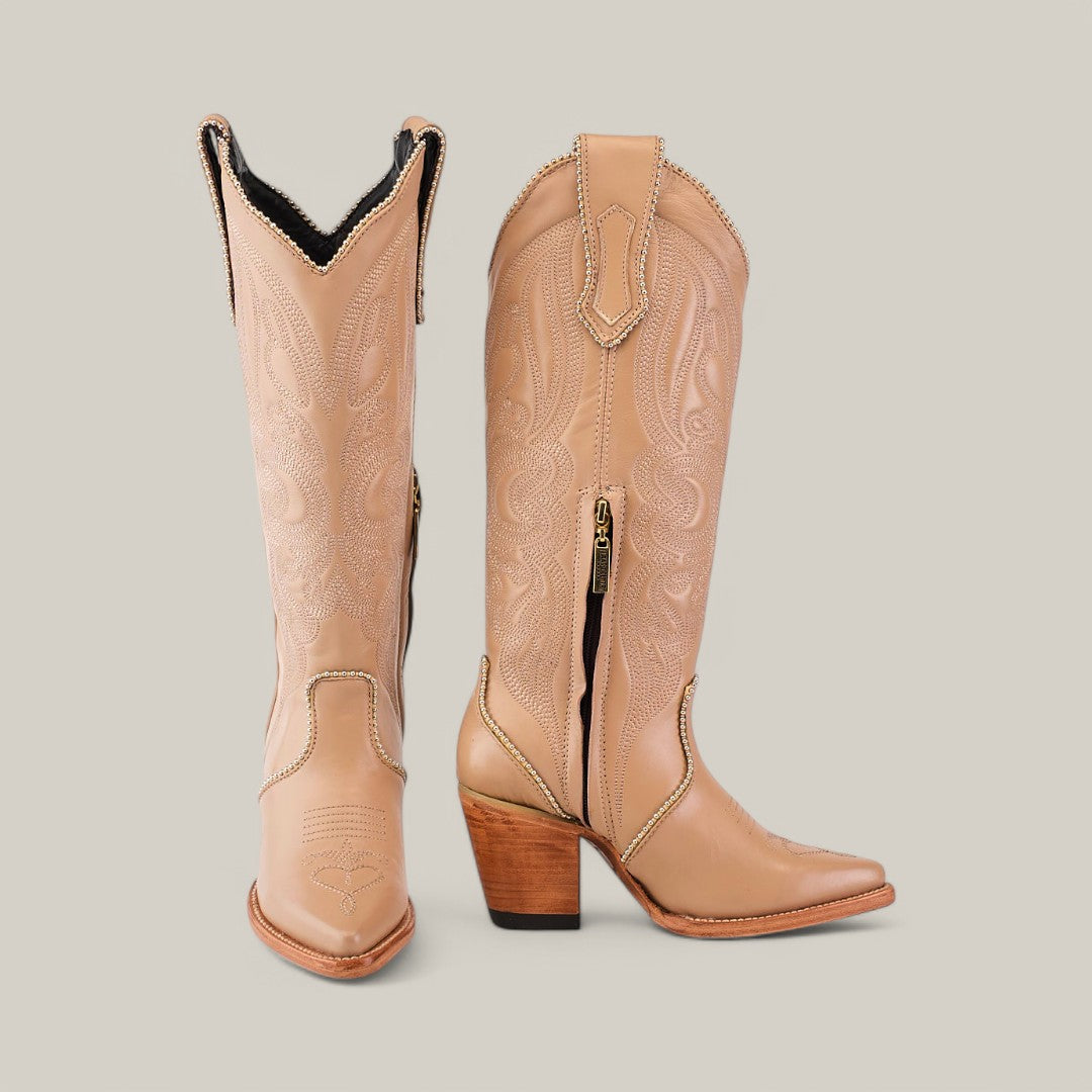 The Linda Studs Tall Shaft Cream - J Toe boots from the Platinum Collection feature intricate embroidery, a pointed toe, stacked wooden heel, and pull tabs. One boot is upright, while the other angles slightly to showcase a side zipper for easy wear.