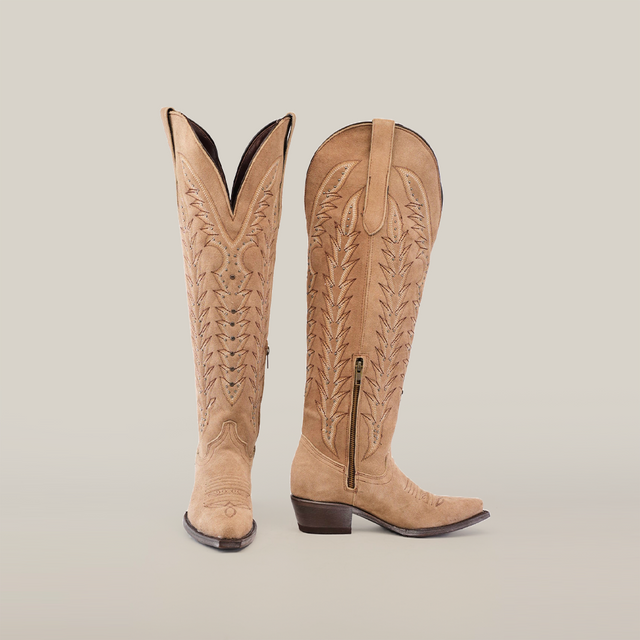 Presenting the Madona Sand Suede boots: a pair of Tall Shaft Snip Toe boots featuring intricate embroidery and side zippers. One boot stands upright, while the other is angled, revealing both front and side views.