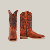 The Rustic Cogñac handcrafted boots, made from premium cowhide leather and featuring intricate black stitching, are displayed on a light background. One stands upright while the other is slightly tilted. They showcase a square toe and stacked leather heel.