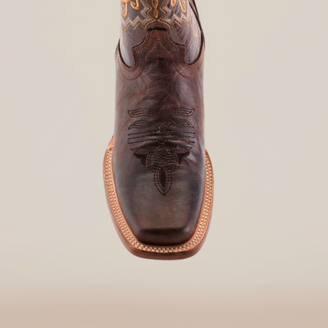 A close-up of the Western Stitch Tabaco Short Shaft boot highlights its exceptional leather and intricate scorpion design on the narrow square toe. The visible stitching around the sole enhances its striking western appeal, all set against a plain white background.