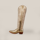 Introducing the Brittany Gold - Tall Shaft - Snip Toe: a handcrafted womens knee-high cowboy boot in metallic gold with intricate stitching, a pointed toe, and a short wooden heel, showcased on a plain gray background.