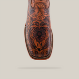 A close-up of the Handtooled Leave Orix - Square Toe cowboy boot highlights its premium cowhide construction with intricate floral patterns, detailed edge stitching, and a polished finish, set against a white background.