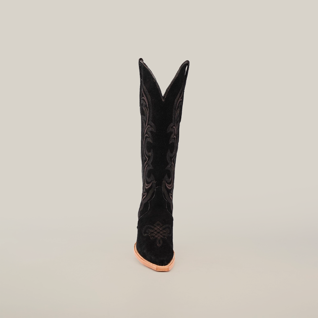 The Amara Black Suede cowboy boot, with intricate stitching, is prominently displayed against a white background. It boasts a snip toe, slightly browned sole, and an elegantly shaped tall shaft with a V-cut opening.