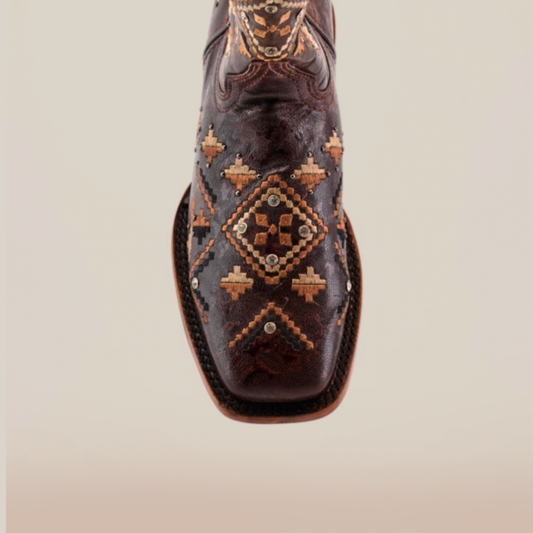 Close-up of Maya Brown Short Shaft Square Toe boots, highlighting intricate geometric embroidery in brown and tan. These premium leather boots feature diamond patterns and small studs for added detail against a plain light beige background.