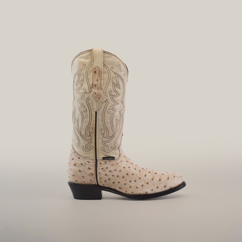 This handcrafted Karoo Ostrich Print Bone boot features a light tan leather upper with intricate stitched patterns and an ostrich print foot. It has a dark brown leather sole and heel, providing a striking contrast to the light finish.