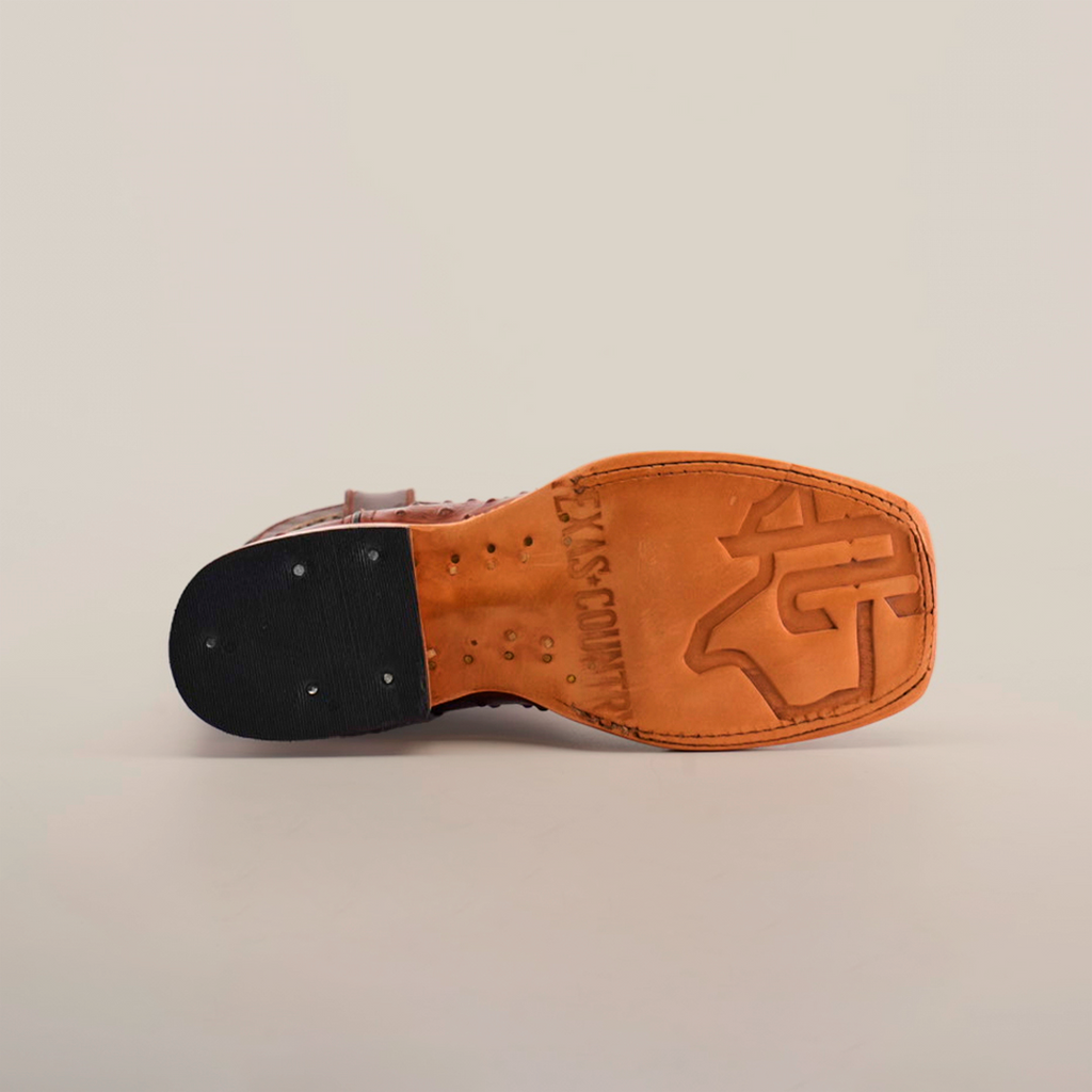 The Karoo Ostrich Print Chocolate Square Toe shoe boasts premium brown leather, a distinct logo, and a well-crafted sole with detailed tacks on the black heel against a white background, all highlighting its quality construction and design elegance.
