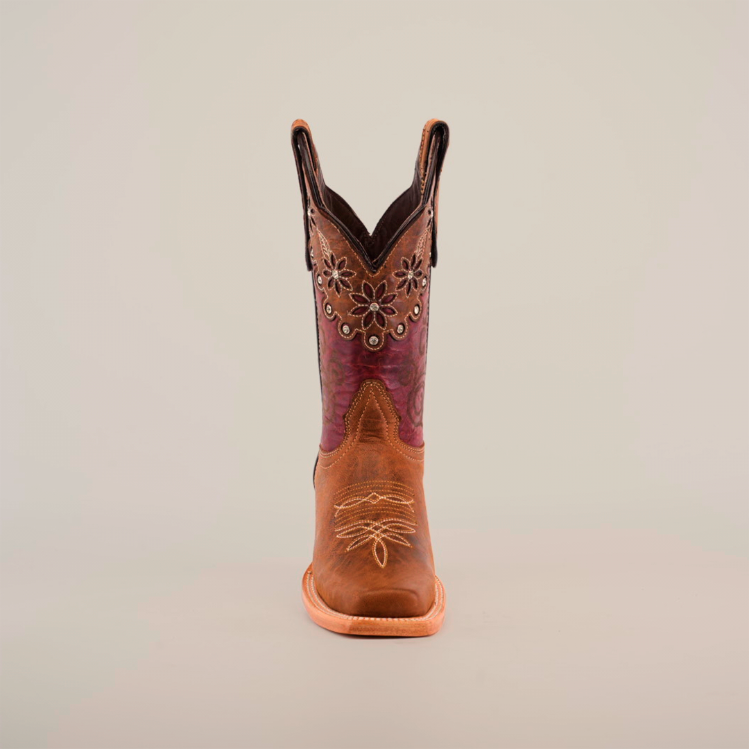 The Grecas Orix cowboy boot, with its narrow square toe, boasts a brown leather exterior adorned with decorative foot stitching and floral upper patterns. Its short shaft combines dark brown and purple leather, showcased upright against a plain white background.