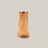 The Prime Suede Honey Square Toe, a single tan leather ankle boot with a hint of cowboy flair, features a brown sole. Seen front-on against a white background, it boasts a stylish red and black pull tab at the top of the opening.