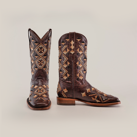 The Maya Brown - Short Shaft - Square Toe cowboy boots feature intricate geometric patterns in premium leather. One boot is upright, the other tilted, highlighting its detailed craftsmanship against a plain background.