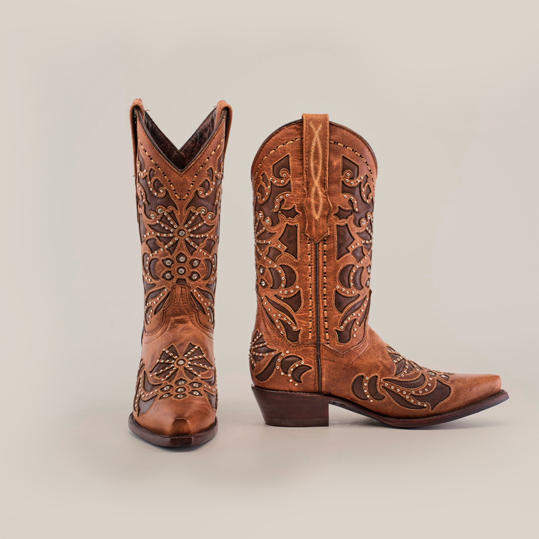 The Cotulla Tabaco Crystals boots feature intricate floral and geometric patterns with decorative studs. One boot stands upright and the other leans sideways against a plain white background, exuding true Western sophistication.