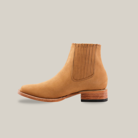 The Prime Suede Honey Square Toe is a tan leather Chelsea boot with a square toe, elastic side panels, and a low stacked wooden heel. It features stitching details around the panels and is set against a white background.