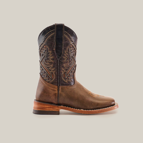 The Ranch Camel Square Toe is a brown leather cowboy boot, showcasing western elegance with intricate stitching and a slightly raised heel. Crafted from premium cowhide, it features a darker shaft adorned with decorative patterns, viewed stylishly from the side.