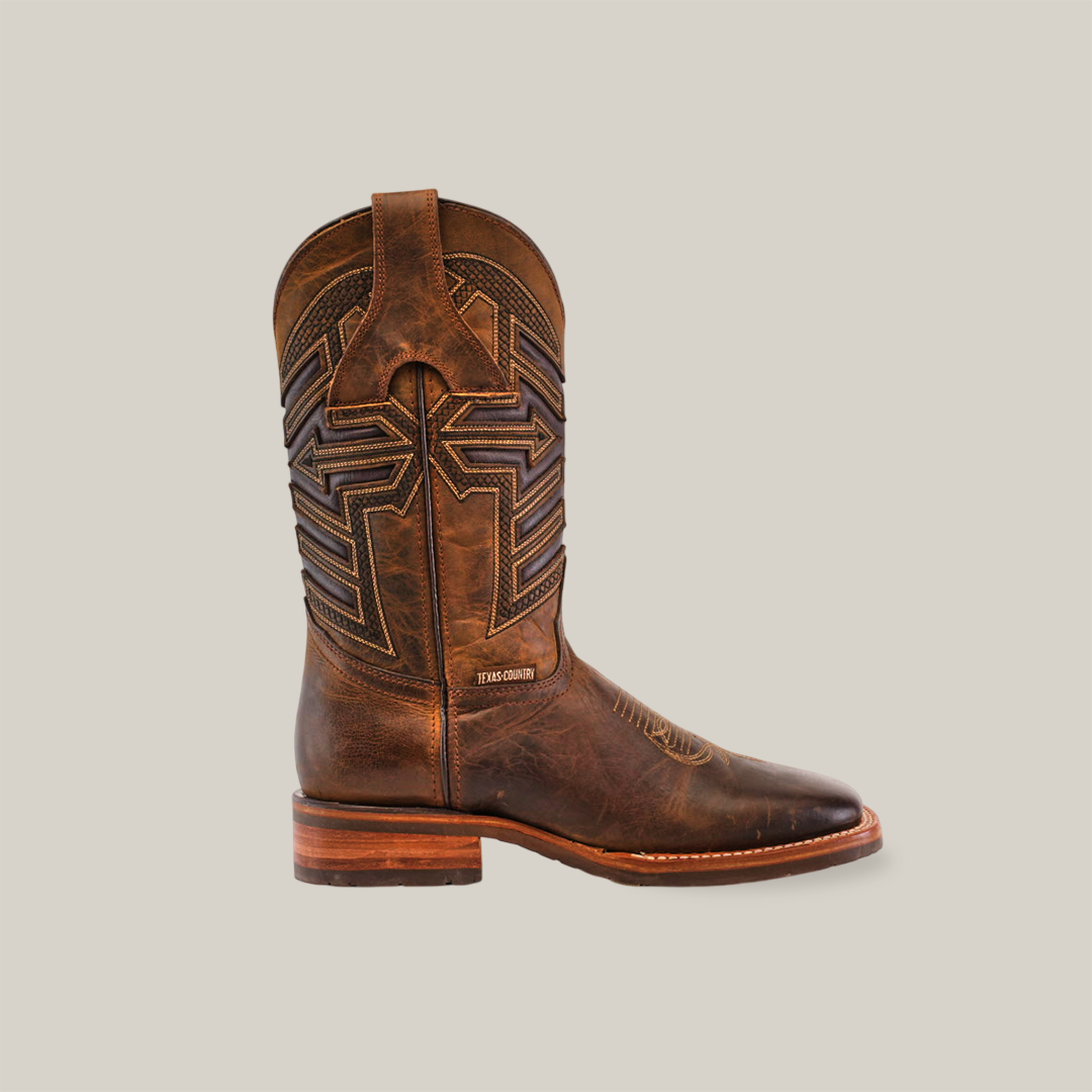 The Azkar Tan cowboy boot features a premium cowhide construction, intricate shaft stitching, a top pull tab, and a low wooden heel. Set against a light beige background, it combines style with practicality with its slip-resistant sole and square toe design.