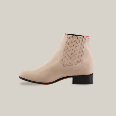 The Prime Suede Pearl Round Toe is a beige suede ankle boot with an elastic side panel and pink back accent. This handcrafted design boasts a rounded toe and low black heel, elegantly showcased on a white background.