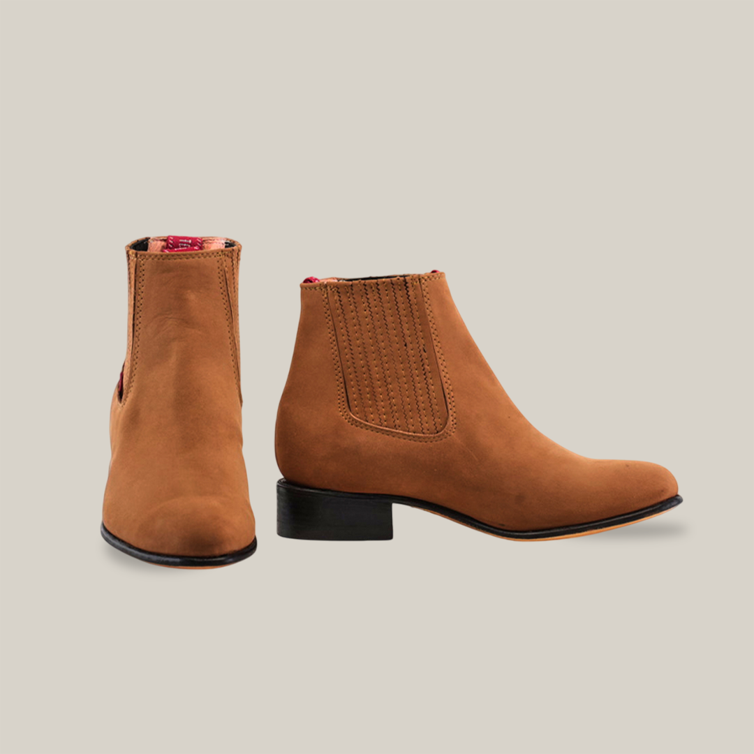 Displayed against a white background, the Prime Suede Sand Round Toe boot stands elegantly. One boot is forward-facing, showing its classic silhouette, while the other reveals a side profile with an elastic panel and low heel—ideal for complementing any cowboy look.