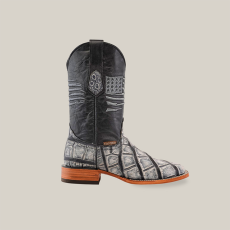 Side view of the American Alligator Print Rustic Black - Square Toe cowboy boot featuring decorative patterns on a black upper, textured gray and black lower resembling alligator print, brown wooden sole, small heel, and displayed against a plain white background.