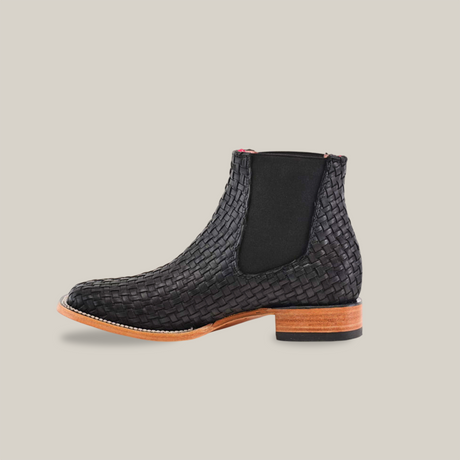 The Basket Weave Black Square Toe ankle boot features a black leather basket weave design, wooden sole, and black elastic side panels with a stylish square toe, all set against a plain white background.