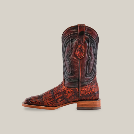 The Gator Print Cogñac boot, elegantly displayed on a plain white background, is handcrafted with rich brown premium cowhide leather in an alligator pattern. It features intricate stitching, a wooden heel, and a square toe design.