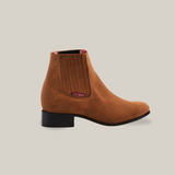 Introducing the Prime Suede Sand Round Toe, a brown marvel with red accents and elastic side panels on a crisp white background. This suede ankle boot features a low black heel, ideal for adding style and flair to any cowboy ensemble.