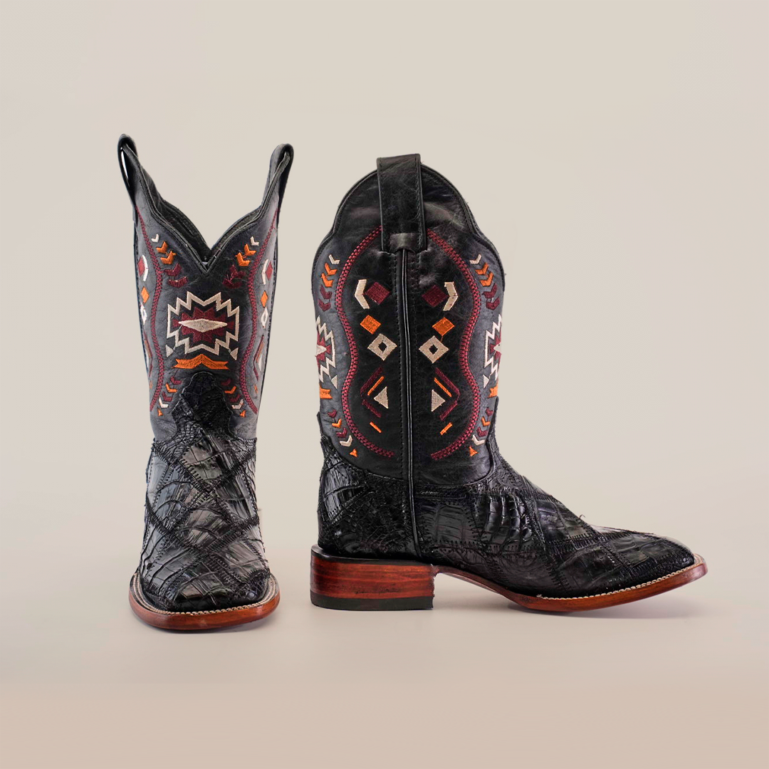 A pair of Exotic American Alligator Patchwork Black Square Toe cowboy boots features intricate multicolored geometric patterns on the shafts, mimicking exotic leather textures. The boots have a wooden sole and a pointed toe, displayed upright on a white background.