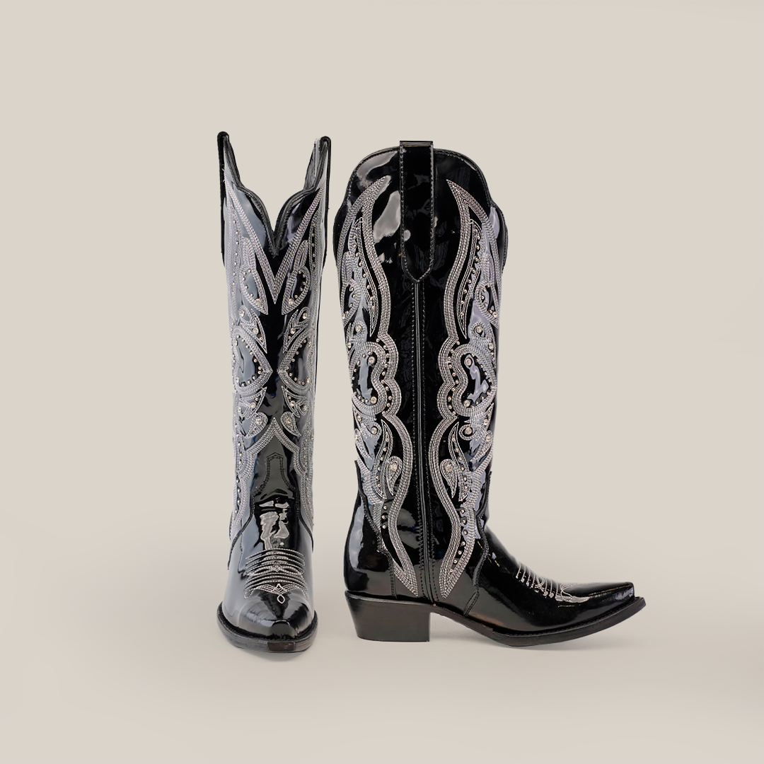 A pair of Artemisa Patent Black boots with a tall shaft, snip toe, and intricate silver embroidery. These shiny, premium leather cowboy boots with a low heel are elegantly displayed against a plain white background.