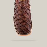 Close-up of the Exotic Piraruco Fish - Matte Brown - Square Toe boot. Crafted from exotic leather with a textured reptile-skin-like design, it features detailed stitching around the sole on a light, neutral background.