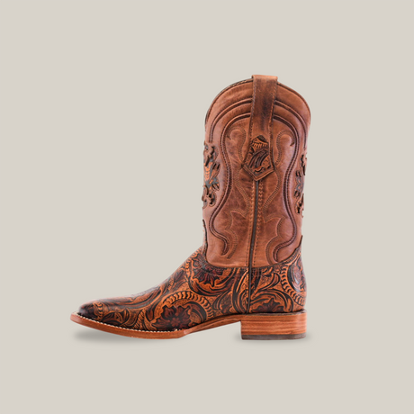 The Handtooled Leave Orix cowboy boot, featuring intricate floral and leave patterns on premium brown cowhide, sports a square toe and low heel. With side pull-tabs, its detailed design covers the entire surface against a plain white background.