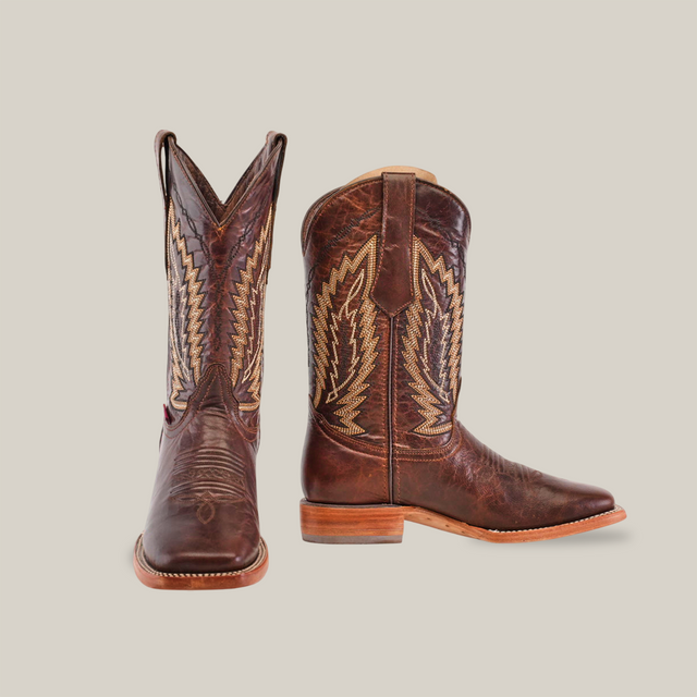 The Dessert Camel - Square Toe cowboy boots are crafted from premium cowhide with intricate stitching. One boot stands upright to highlight its side pattern, while the other is angled to display its square toe. Both have wooden heels and light-colored soles, exuding timeless elegance on a white background.