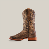 The Rustic Camel Brown boot features premium cowhide leather, intricate stitching, a wooden heel, and decorative patterns. This Western-style boot has a square toe and offers safety with its slip-resistant sole against a white background.