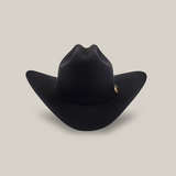 Against a plain white backdrop, the 6X Real Black cowboy hat with a wide brim and pinched crown stands proudly, featuring a small pin on the side that echoes the classic style of a Larry Mahan hat.