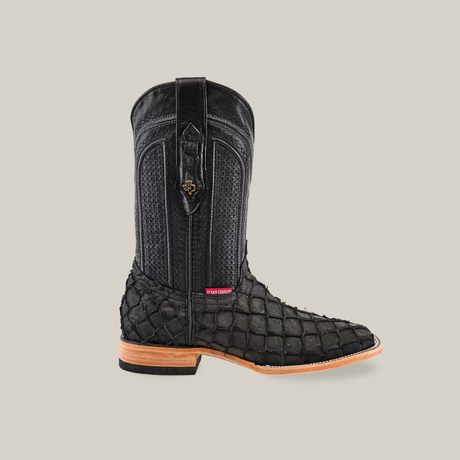 An Exotic Piraruco Fish boot in matte black stands upright against a white background, featuring a textured, scaled surface, square toe, wooden sole, intricate stitching, decorative pull tab, and emblem in authentic leather.