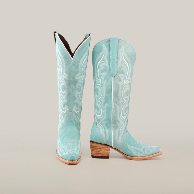 The Amara BB Suade boots feature a tall turquoise shaft with intricate white stitching, an elegant snip toe, and a stacked wooden heel, beautifully showcased against a plain white background.