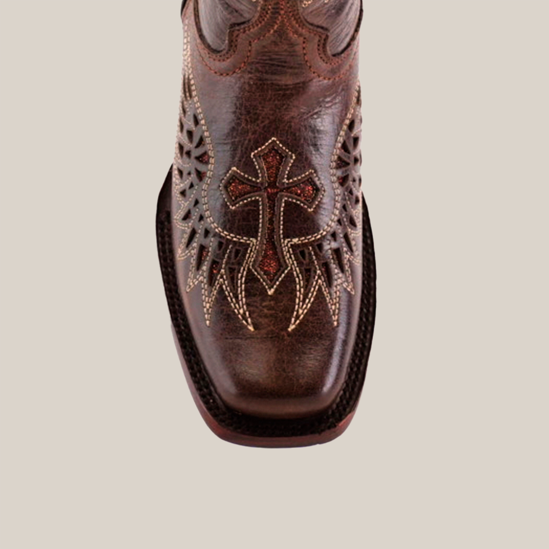 A close-up of the Texas Cross Glitterbomb Brown boot reveals masterful artistry with intricate embroidery and decorative stitching on premium leather. This narrow square toe boot highlights a prominent cross design, set against a plain white background.