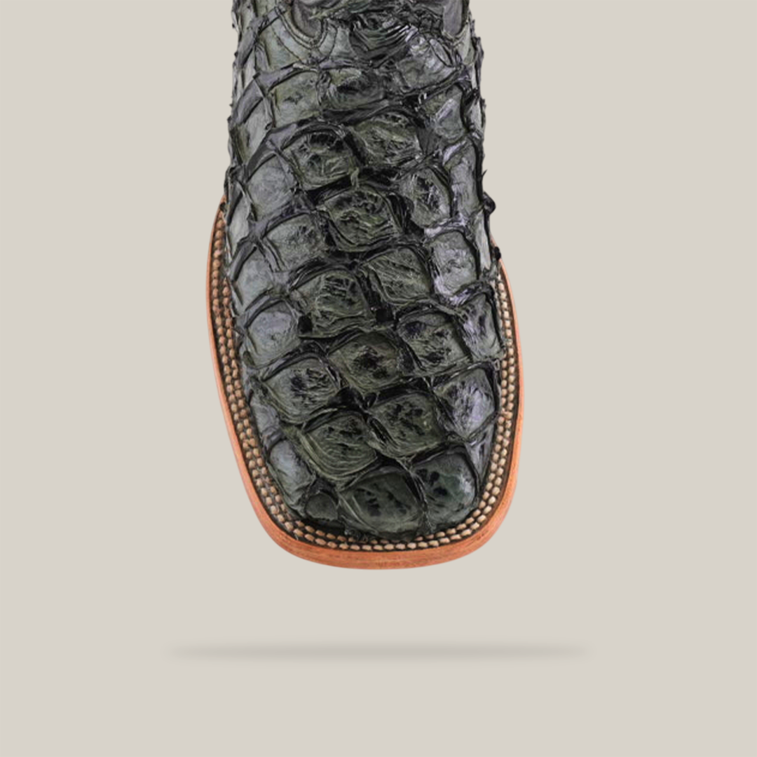 Close-up of an Exotic Piraruco Fish - Charcoal- Square Toe boot, loved by fashion enthusiasts, showcasing a glossy dark green fish leather pattern. It features a light brown sole with detailed edge stitching, set against a plain white background.