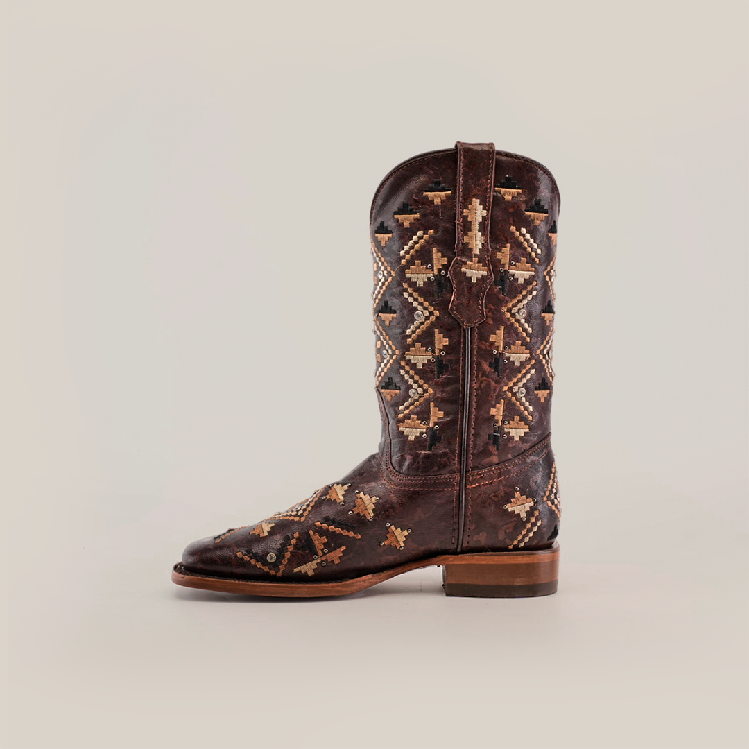 The Maya Brown Short Shaft boots feature premium leather and intricate tan and beige geometric embroidery on the shaft and foot, with a square-toe design and wooden heel. They are elegantly displayed against a plain light background.