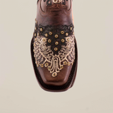 A close-up of the Faenza Crystals Brown cowboy boot reveals premium leather with intricate black and white embroidery on the toe, featuring floral and geometric designs, accented by metallic studs. The boot showcases a stylish narrow square toe shape.