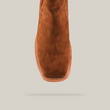 The Prime Suede Caramel Square Toe boot, featuring a square toe and visible white stitching around the sole, exudes Western charm in caramel brown suede. Its centered against a plain white background.