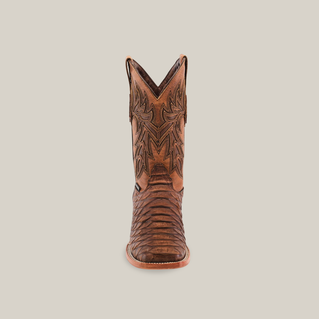 The Jumbo Python Print Rustic Brown boot, centered on a white background, showcases intricate stitched patterns and a square toe. Its decorative leather texture and slightly raised heel embody timeless western charm.