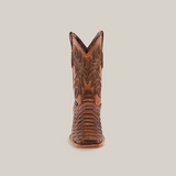 The Jumbo Python Print Rustic Brown boot, centered on a white background, showcases intricate stitched patterns and a square toe. Its decorative leather texture and slightly raised heel embody timeless western charm.