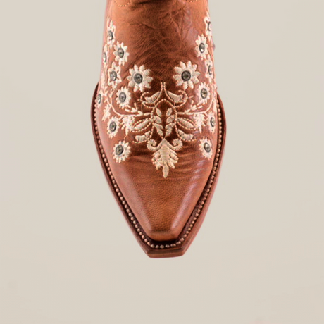 Brown cowboy boot with white floral embroidery and crystal embellishments, adding sparkle. This western style boot features a snip toe and decorative stitching, reminiscent of the Abril Crystals - Mid Shaft boots, set against a plain white background.