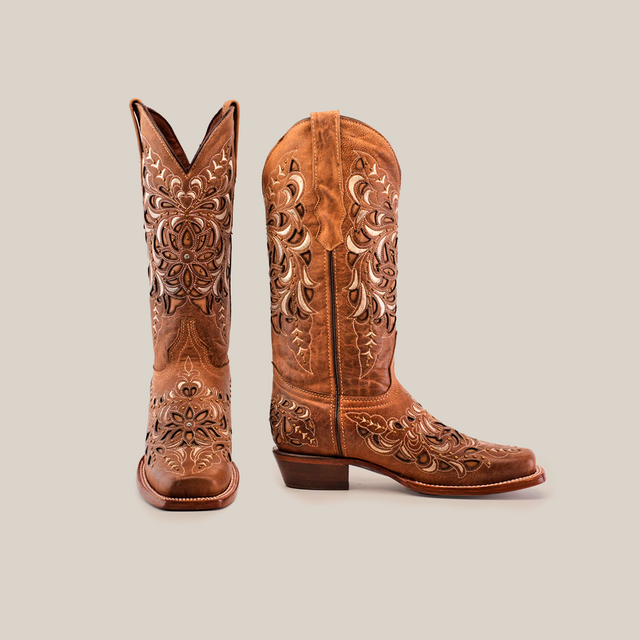 The Kiara Crystals Fawn boots, with a mid shaft and narrow square toe, are adorned with intricate floral embroidery. Crafted from premium brown leather, one boot stands upright while the other tilts gracefully against a pristine white background.