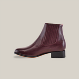 Side view of the Napa Wine - Round Toe, a burgundy leather ankle boot with a low black heel. It boasts calidad excepcional, featuring elastic side panels for easy wear and a smooth, polished finish.