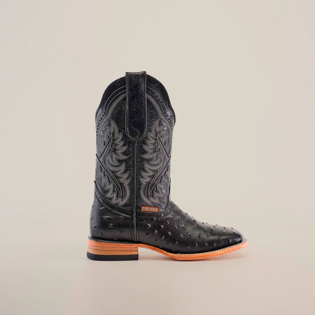 Side view of the Karoo Ostrich Print Black Square Toe cowboy boot, showcasing intricate embroidery on the shaft, textured designs with an ostrich print on the lower part, a light brown sole, small heel, and modern square toe against a plain white background.