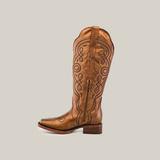 The Eden Copper Tall Shaft boot in premium brown leather features intricate swirl embroidery, a low heel, and a side zipper. It stands upright against a plain white background, highlighting luxury craftsmanship.